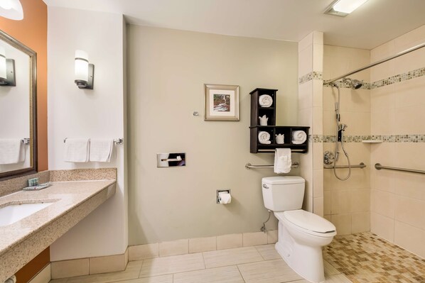 A bathroom with a sink, toilet, and shower. There is a towel rack, a framed picture on the wall, and a shelf with towels.