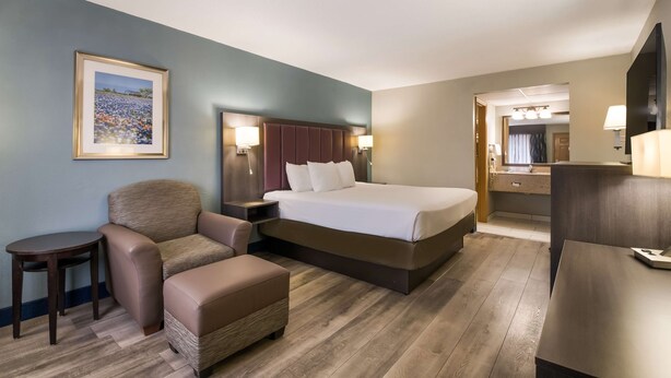 A hotel room with a bed, a chair, a small table, a desk, and a mirror.