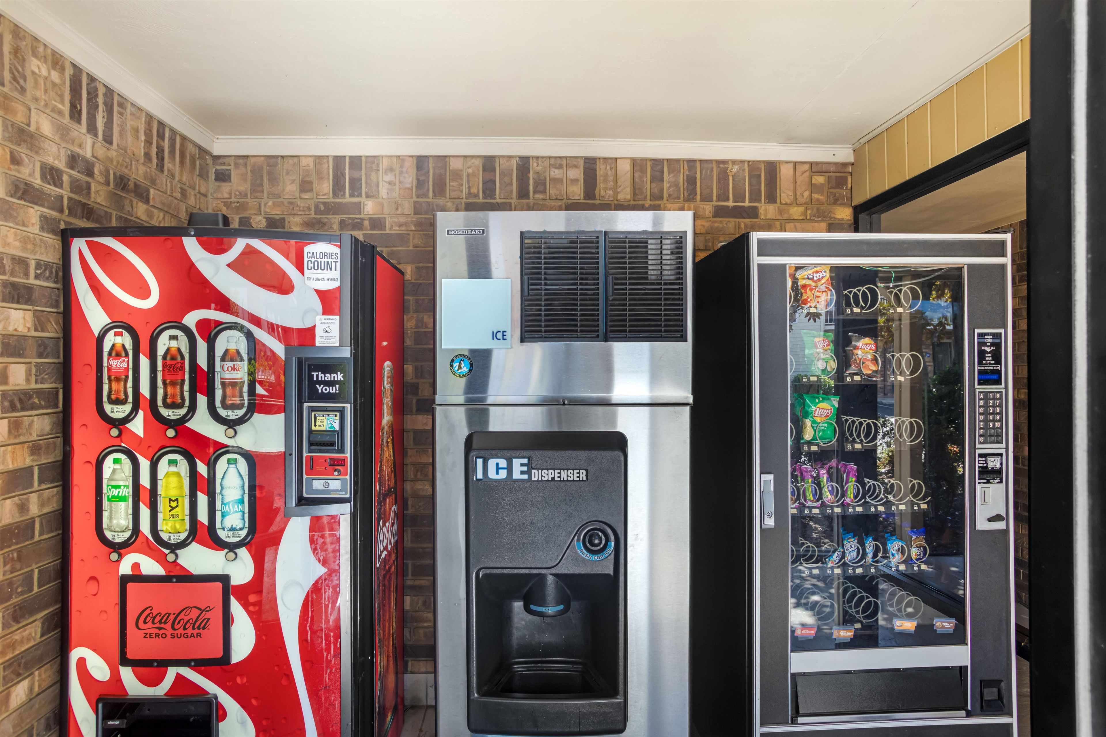 Drei Getränkespender: einer mit Coca-Cola-Branding, einer von Hoshizaki und ein Verkaufsautomat mit Snacks.