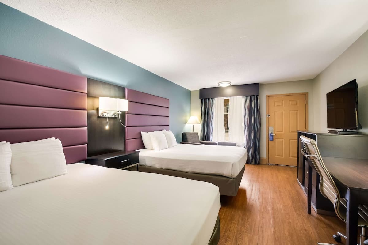 A hotel room with two beds, a desk, a chair, a TV, and a door.
