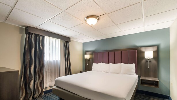 A hotel room with a large bed, a nightstand with a lamp, a headboard, and a window with curtains.