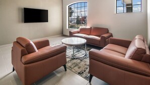 A modern living room with leather sofas, a glass coffee table, and a flat-screen TV mounted on the wall. - Quality Inn & Suites  Fort Worth - Fossil Creek (Fort Worth)