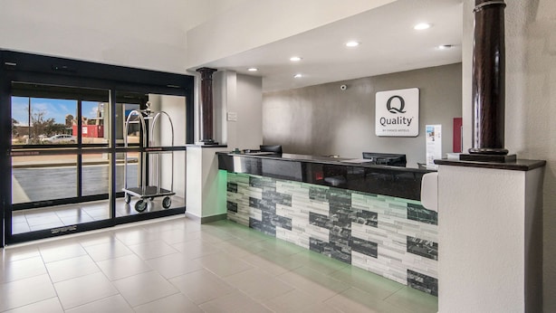 A hotel reception area with a modern design, featuring a reception desk, a sign indicating 'Quality by Choice Hotels', and a view through the glass doors. - Quality Inn & Suites  Fort Worth - Fossil Creek (Fort Worth)
