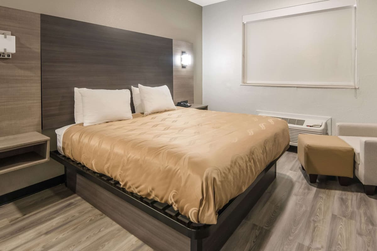Ein modernes Hotelzimmer mit einem großen Bett, einem Nachttisch, einem Sessel und einer fest installierten Klimaanlage.