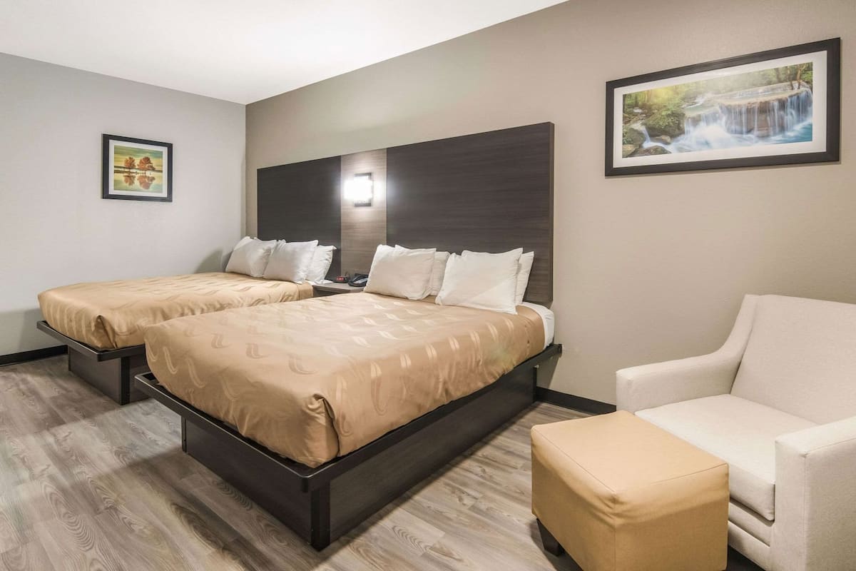 Ein Hotelzimmer mit zwei Betten, einem Schlafsofa, einem Sessel und Bildern an der Wand.
