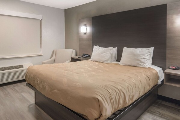 Une chambre d’hôtel moderne avec un grand lit, une table de chevet avec une lampe, une chaise et une grande fenêtre.