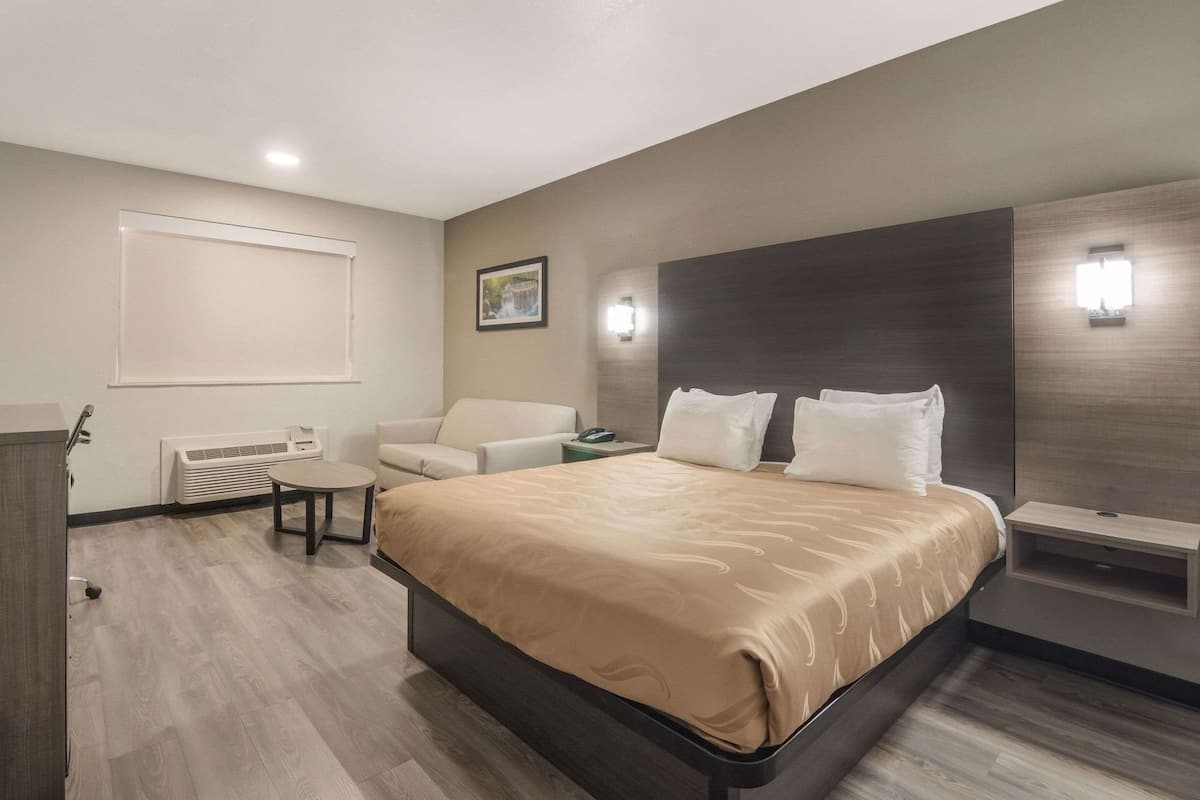 Ein Hotelzimmer mit einem großen Bett, einem Schreibtisch, einem Sessel, einem Nachttisch und einer Wandleuchte.