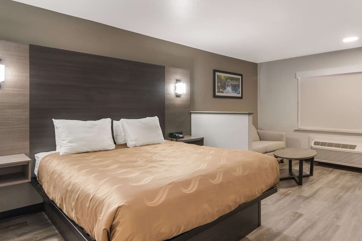 Ein Hotelzimmer mit einem großen Bett, einem Nachttisch, einem Sessel, einem kleinen Tisch und einer Wand-Klimaanlage.