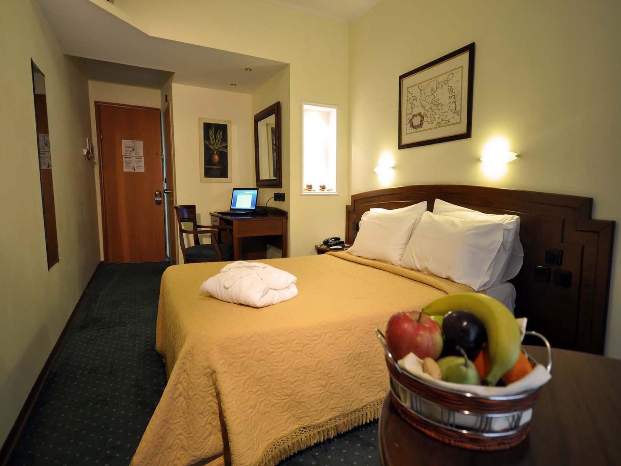 A hotel room with a bed, a desk with a computer, a chair, a wall-mounted map, and a fruit bowl.