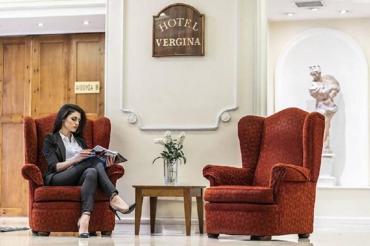 A hotel lobby with a wooden wall, a sign reading 'HOTEL VERGINA,' and a statue in the background.