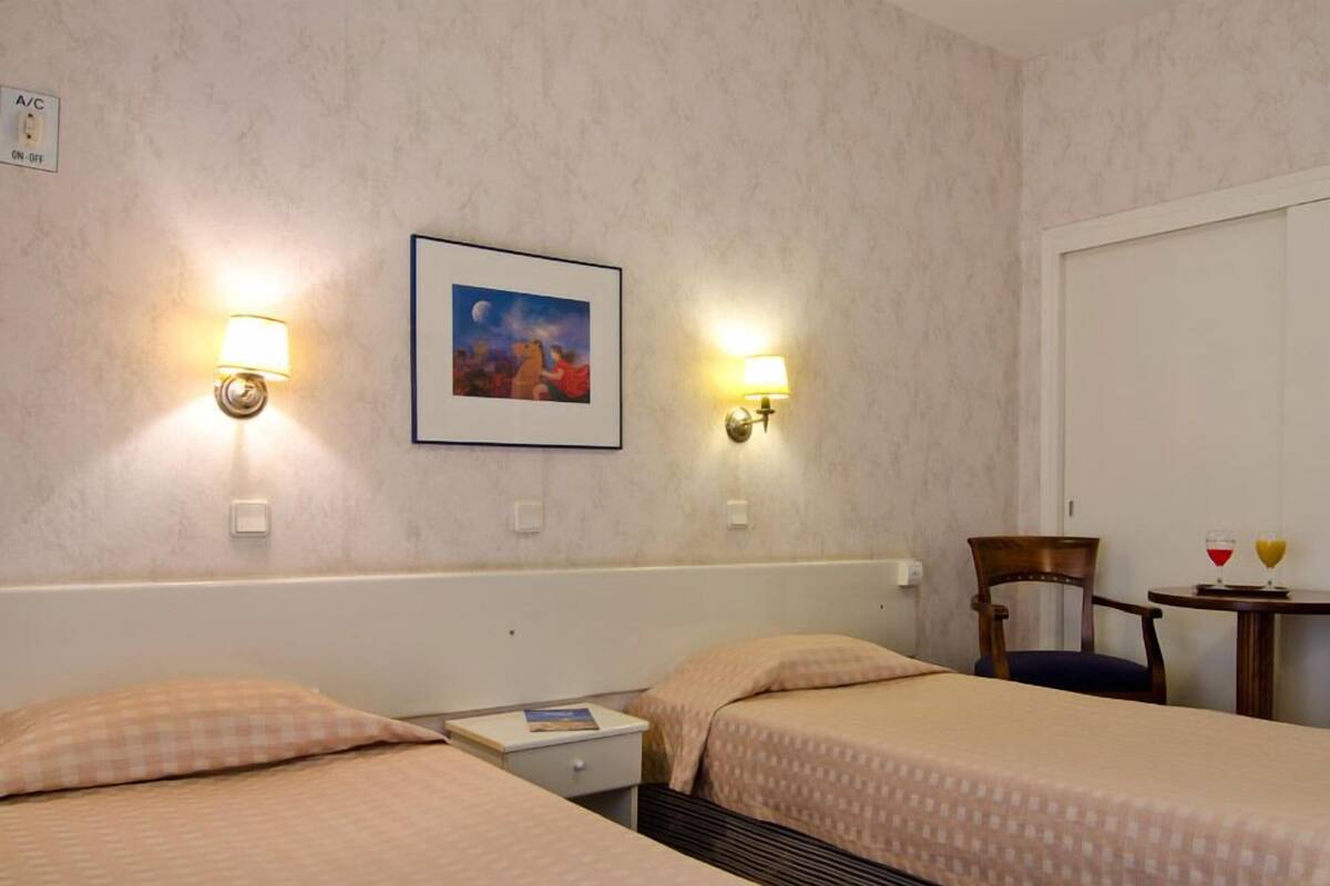 A hotel room with two beds, a nightstand, a chair, and a small table with two drinks.