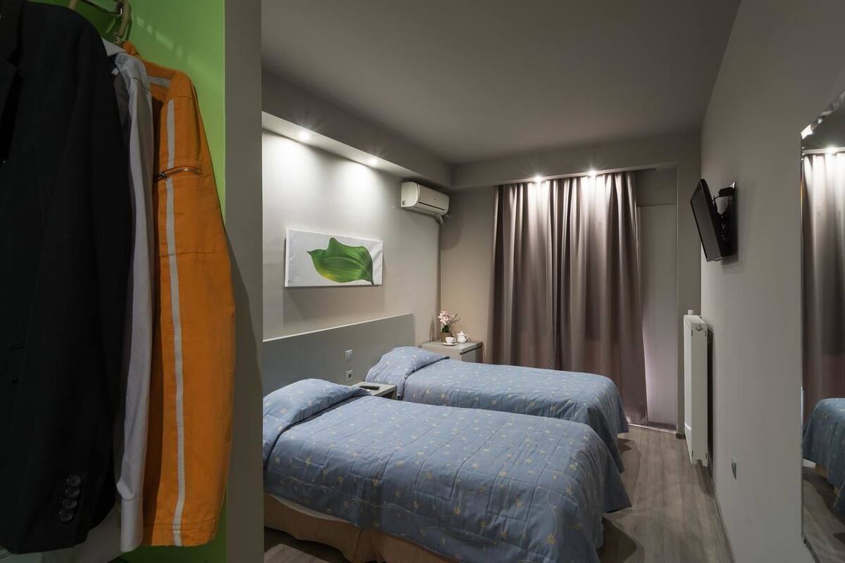 A hotel room with two beds, a flat-screen TV, an air conditioning unit, and a green wall with a leaf decoration.