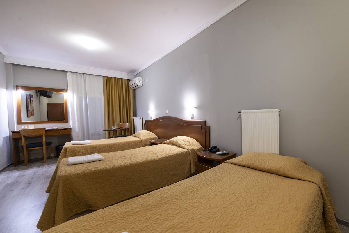 A hotel room with two single beds, a desk with a chair, a small table, a mirror, and a radiator.