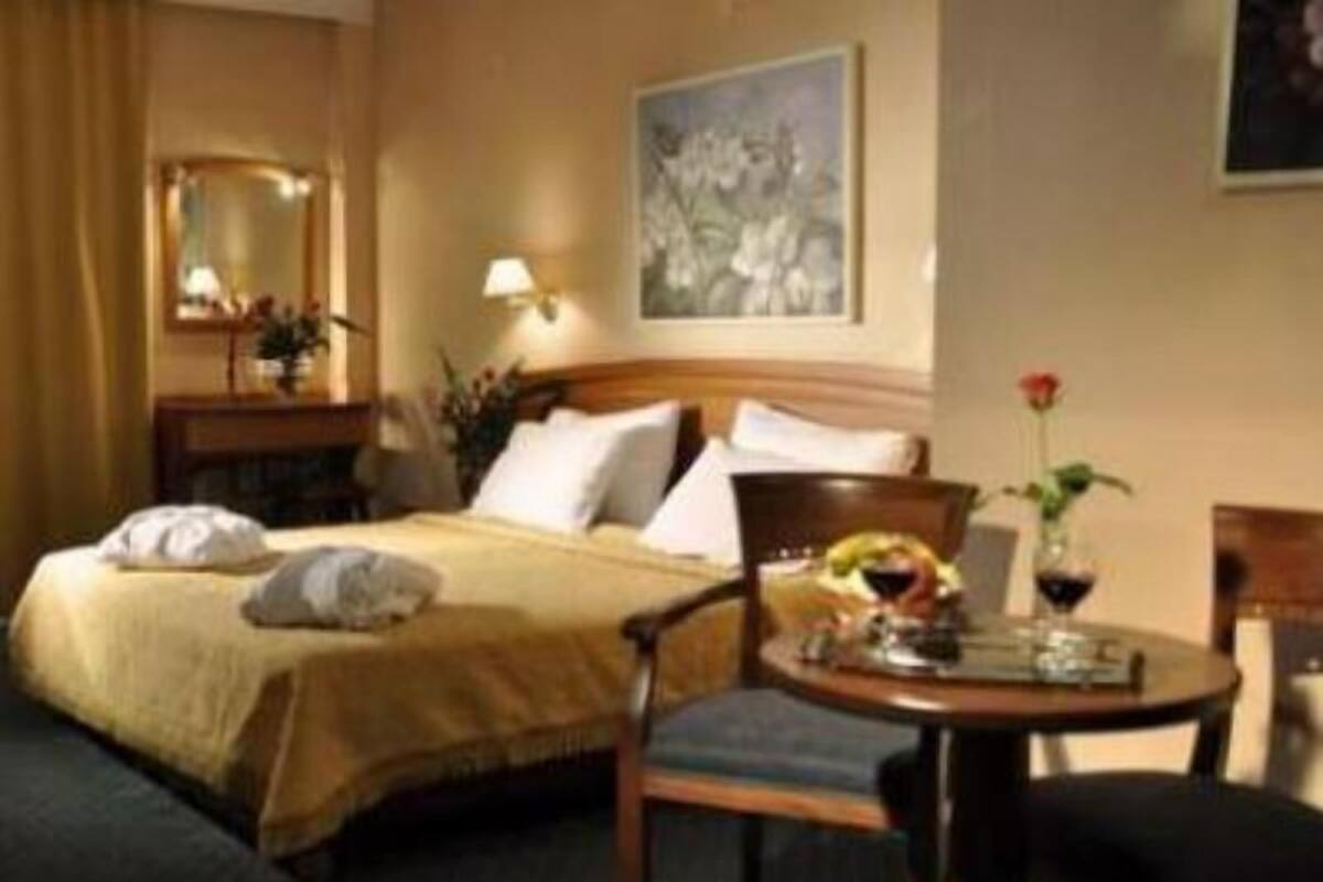 A hotel room with a bed, a chair, a table with a vase of flowers, a lamp, and a painting on the wall.