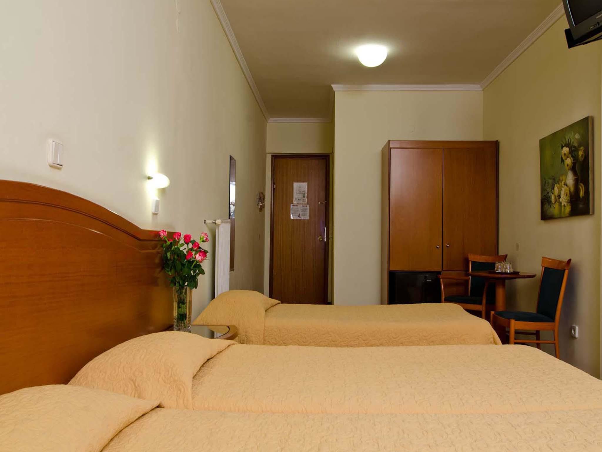 A hotel room with two beds, a desk with a chair, a wardrobe, and a painting on the wall.
