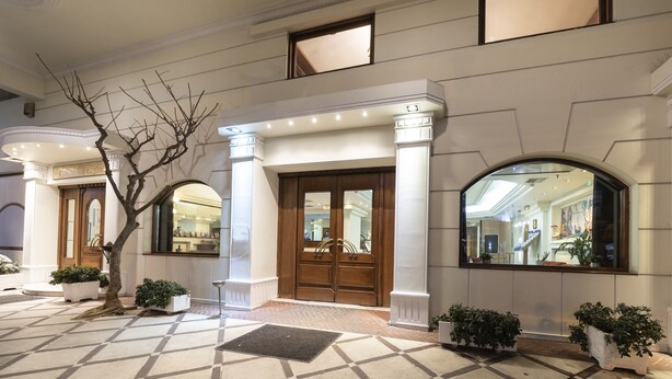 L’entrée d’un hôtel, avec une grande porte en bois, des colonnes blanches et un sol carrelé.