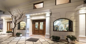 Una entrada de hotel con una puerta de madera imponente, columnas blancas y suelo de baldosas.