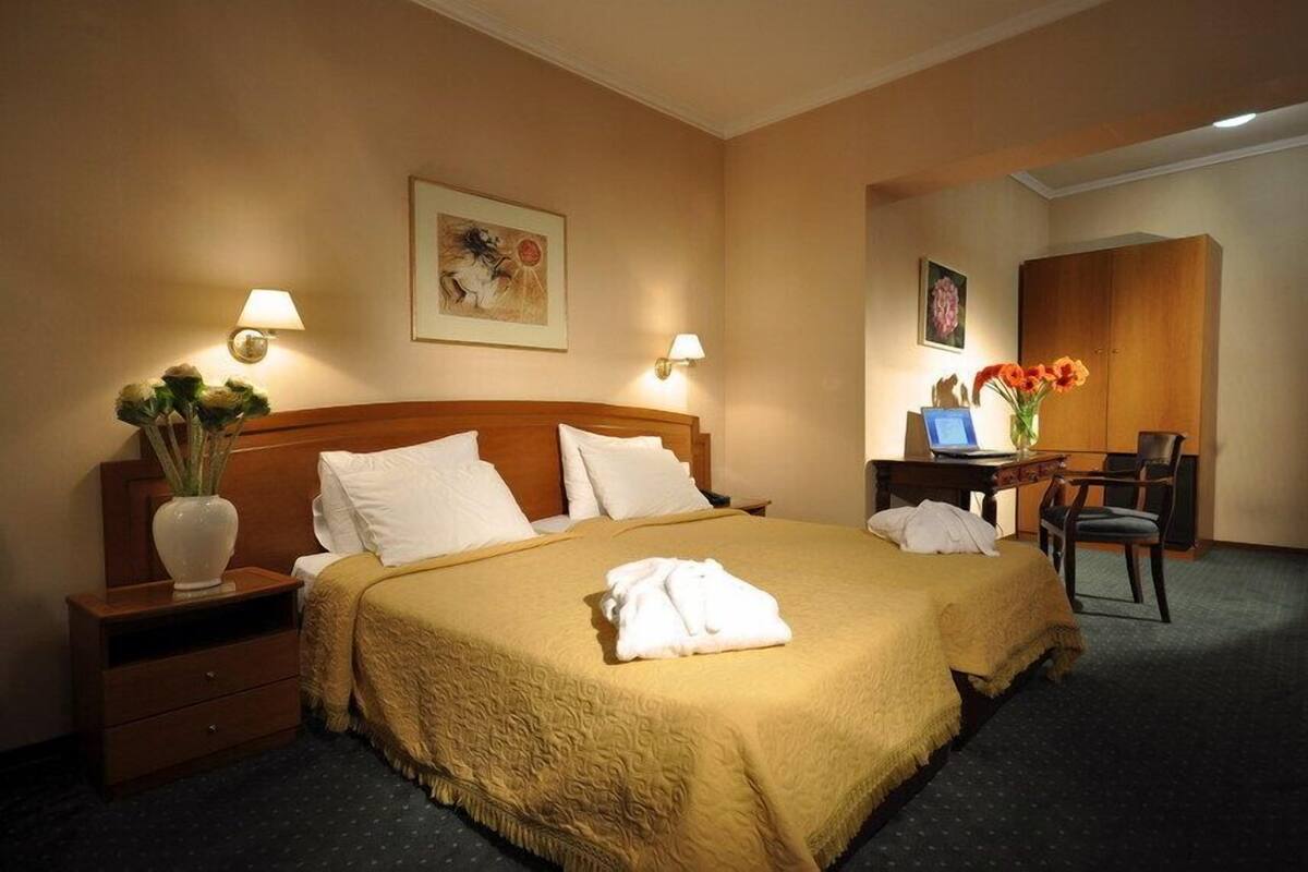 A hotel room with a large bed, two bedside tables, a desk with a chair, and a wardrobe.