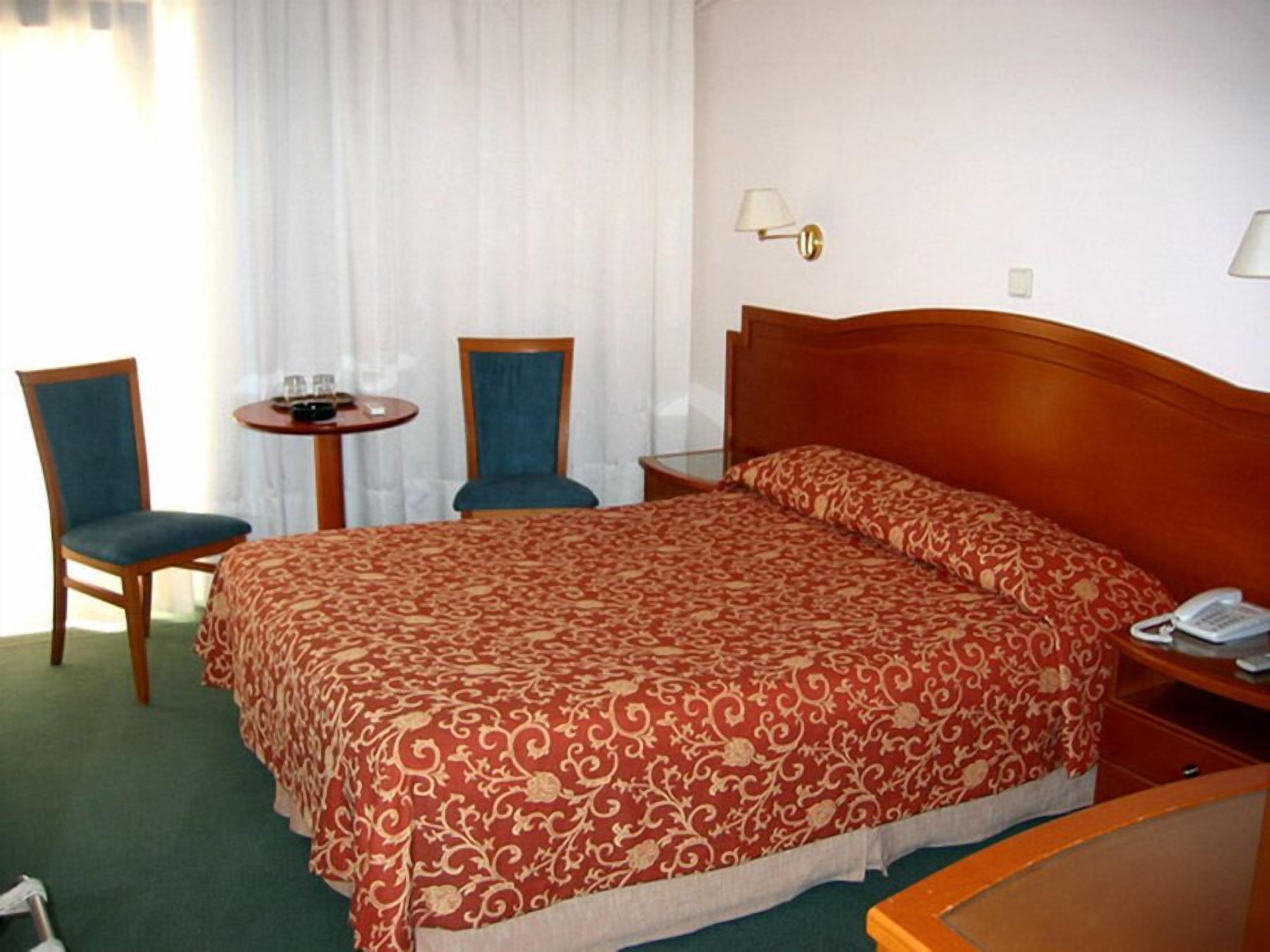 Una habitación de hotel con una cama grande, dos sillones, una mesita y un teléfono en la mesita de noche.