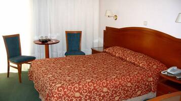 Una habitación de hotel con una cama grande, dos sillones, una mesita y un teléfono en la mesita de noche.