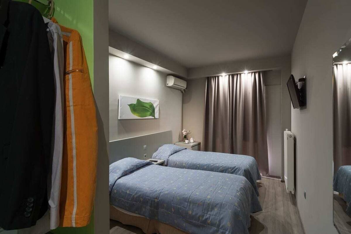 A hotel room with two beds, a wall-mounted TV, an air conditioning unit, and a window with curtains.