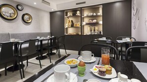 Un comedor moderno con sillas negras, mesas blancas y una mesa para el desayuno con huevos, tostadas y jugo.