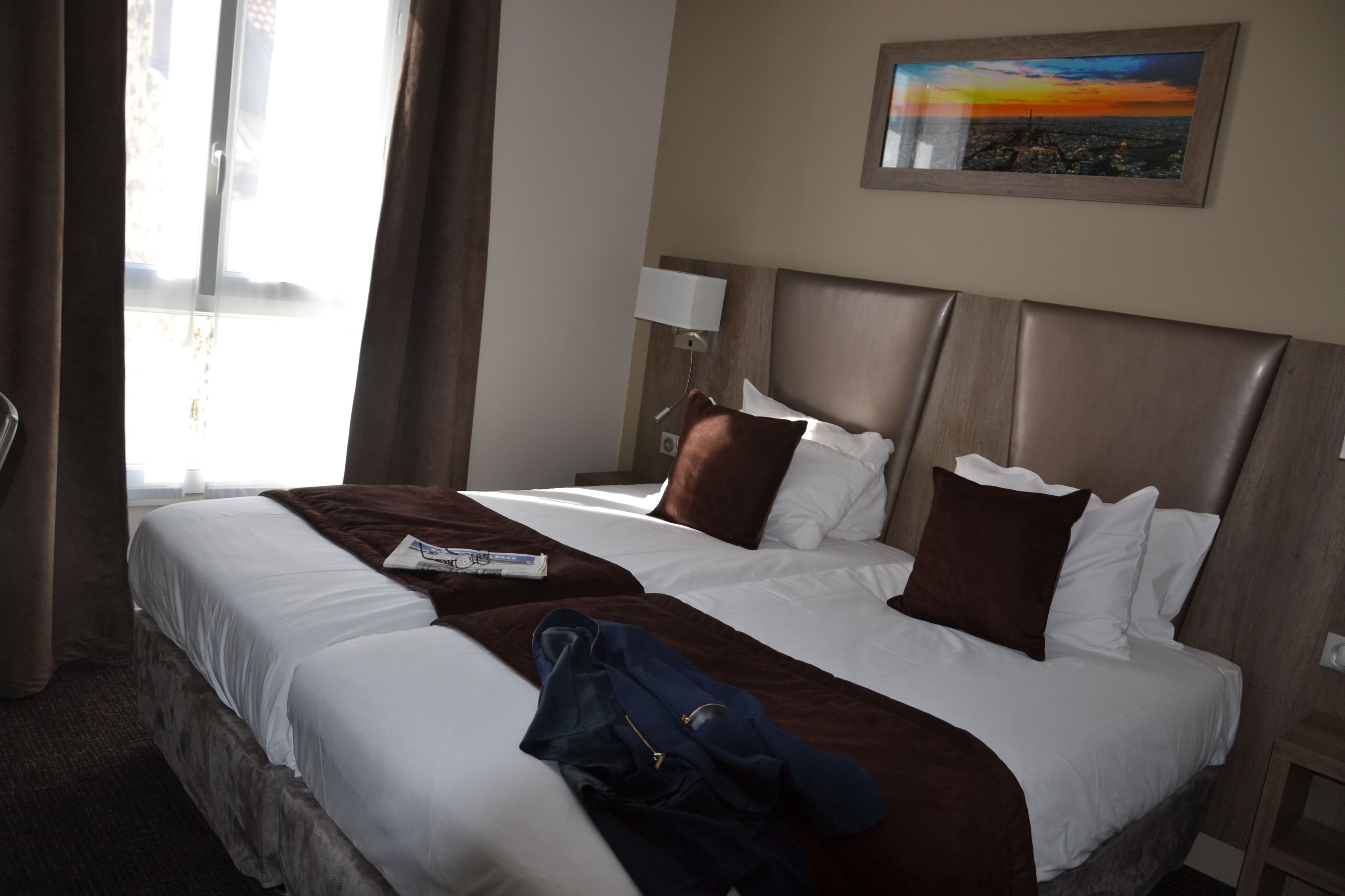 A hotel room with two beds, a nightstand, a lamp, and a painting on the wall.