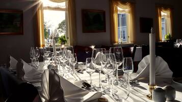 Una mesa de comedor dispuesta con varias copas de vino, platos y cubiertos, con una vela y saleros y pimenteros sobre la mesa.