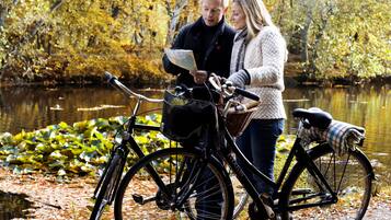 A couple standing by a bicycle with a map, near a body of water surrounded by autumn foliage.