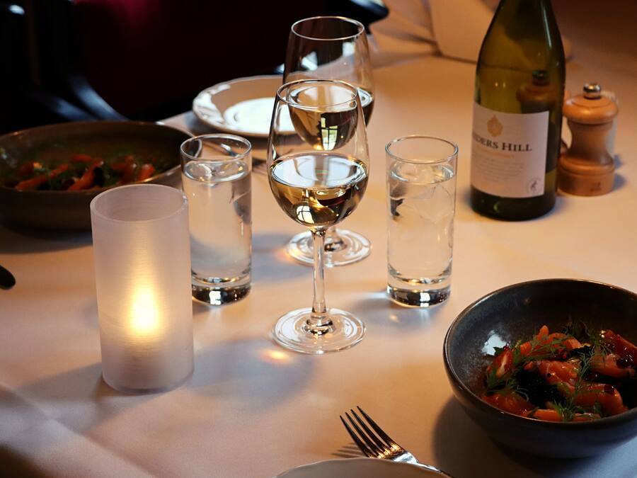 Una mesa de comedor con una vela, copas de vino, una botella de vino y un bol de comida.