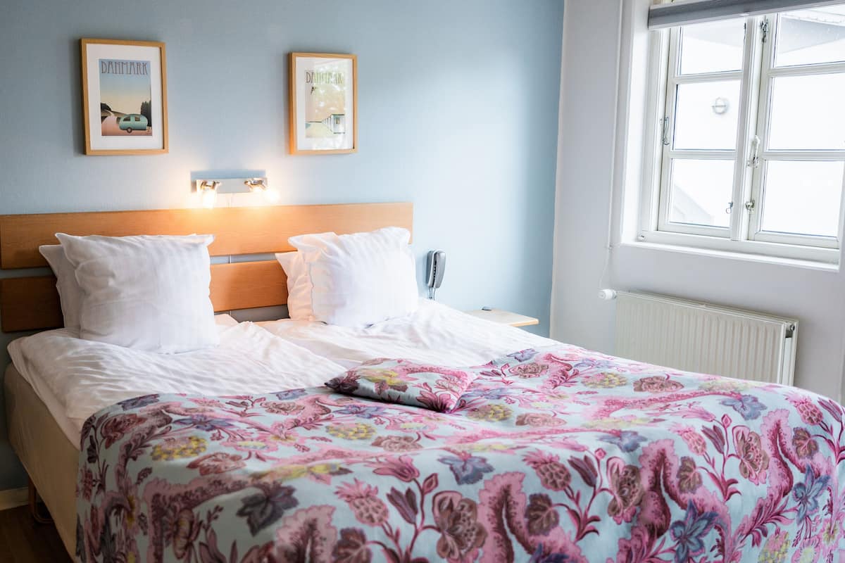 A neatly made bed with a floral bedspread, a wooden headboard, and two framed pictures on the wall.
