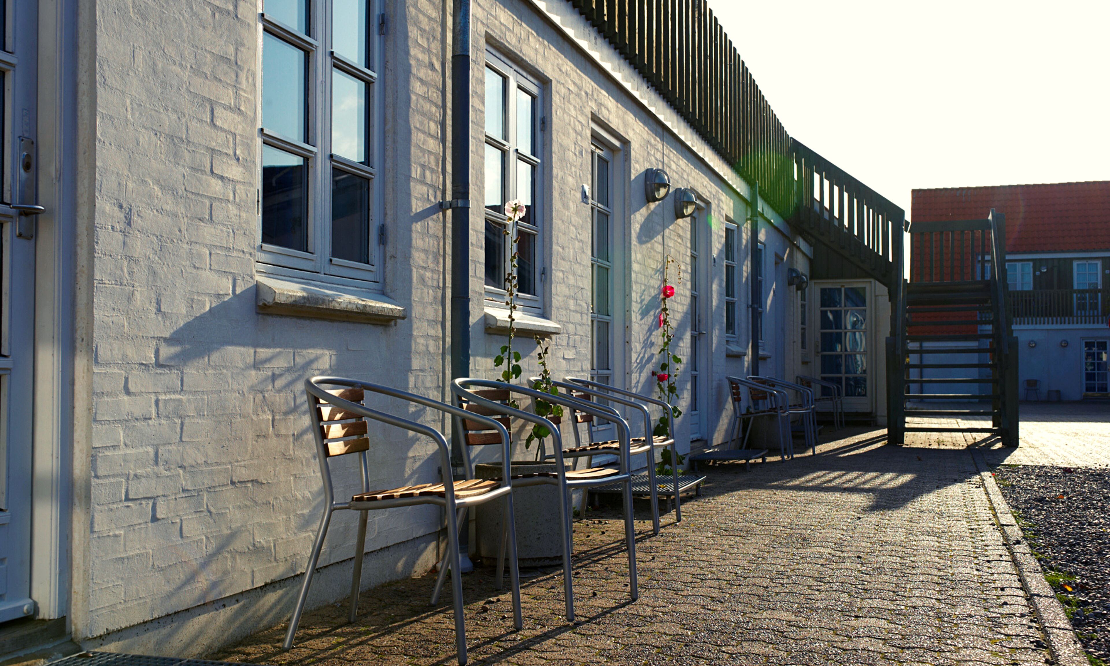 A building with a brick facade, multiple windows, and outdoor seating with metal chairs and tables.