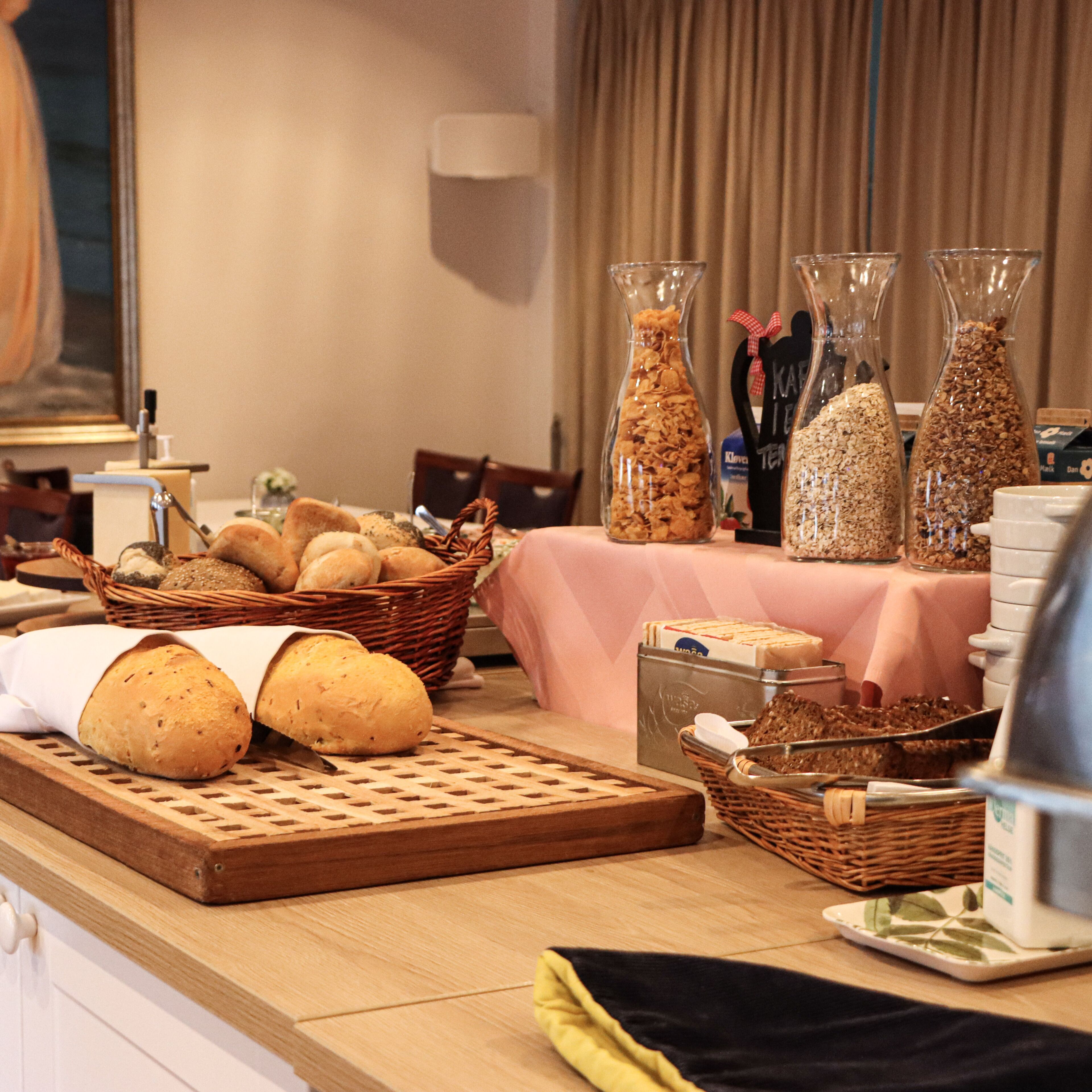 A buffet table with various food items, including breads, pastries, and cereal in glass jars.