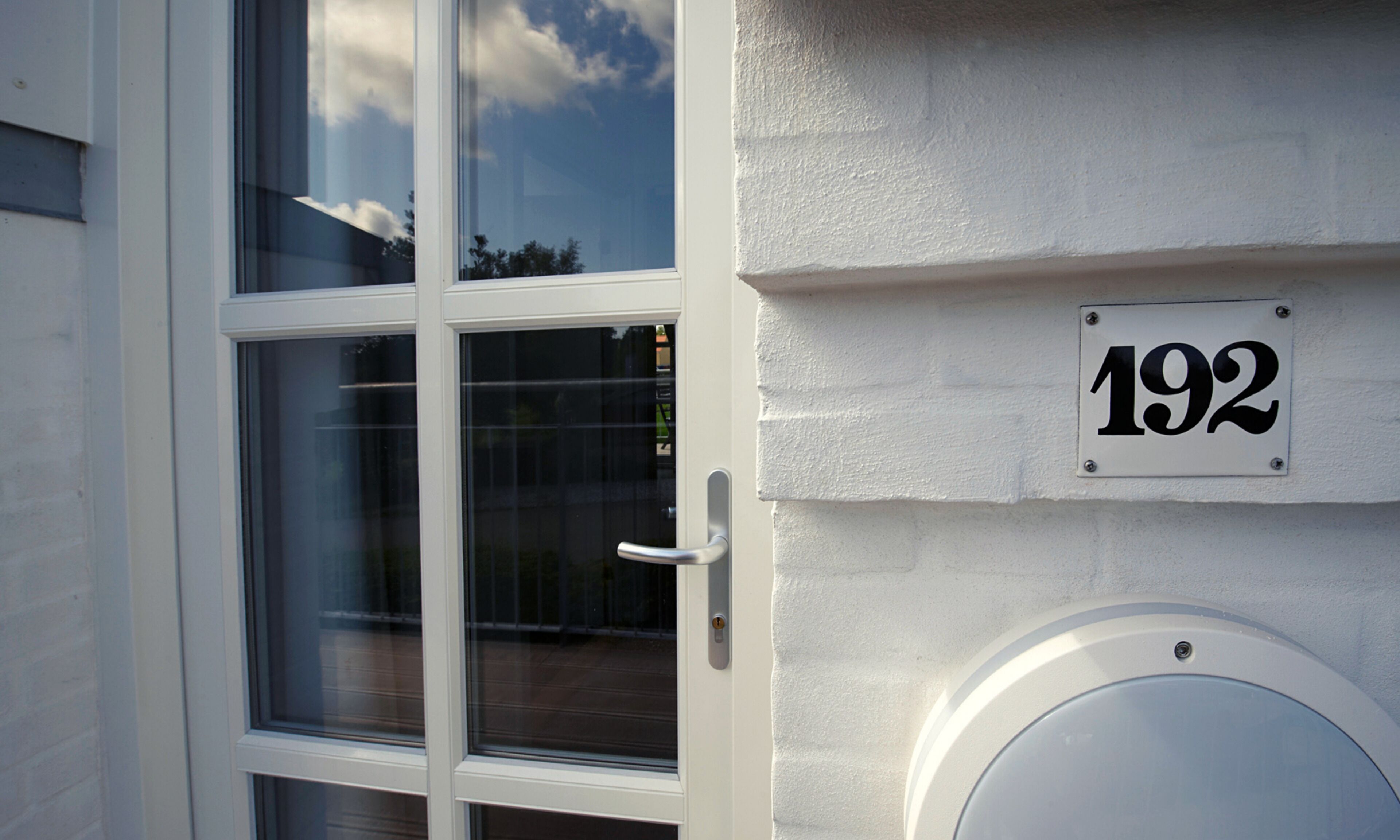 A white building with a glass door and a number plate displaying '192'.