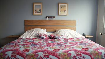 Un dormitorio con cabecera de madera, dos mesitas de noche, colcha con estampado floral y dos cuadros en la pared.