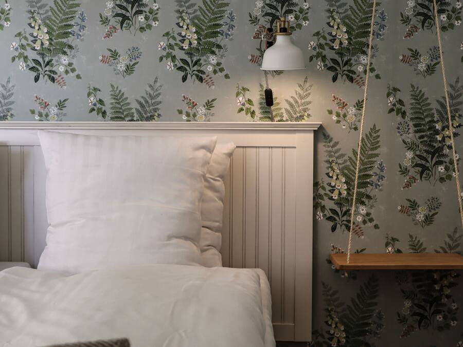 A bedroom with a bed, a hanging lamp, and a wooden shelf.