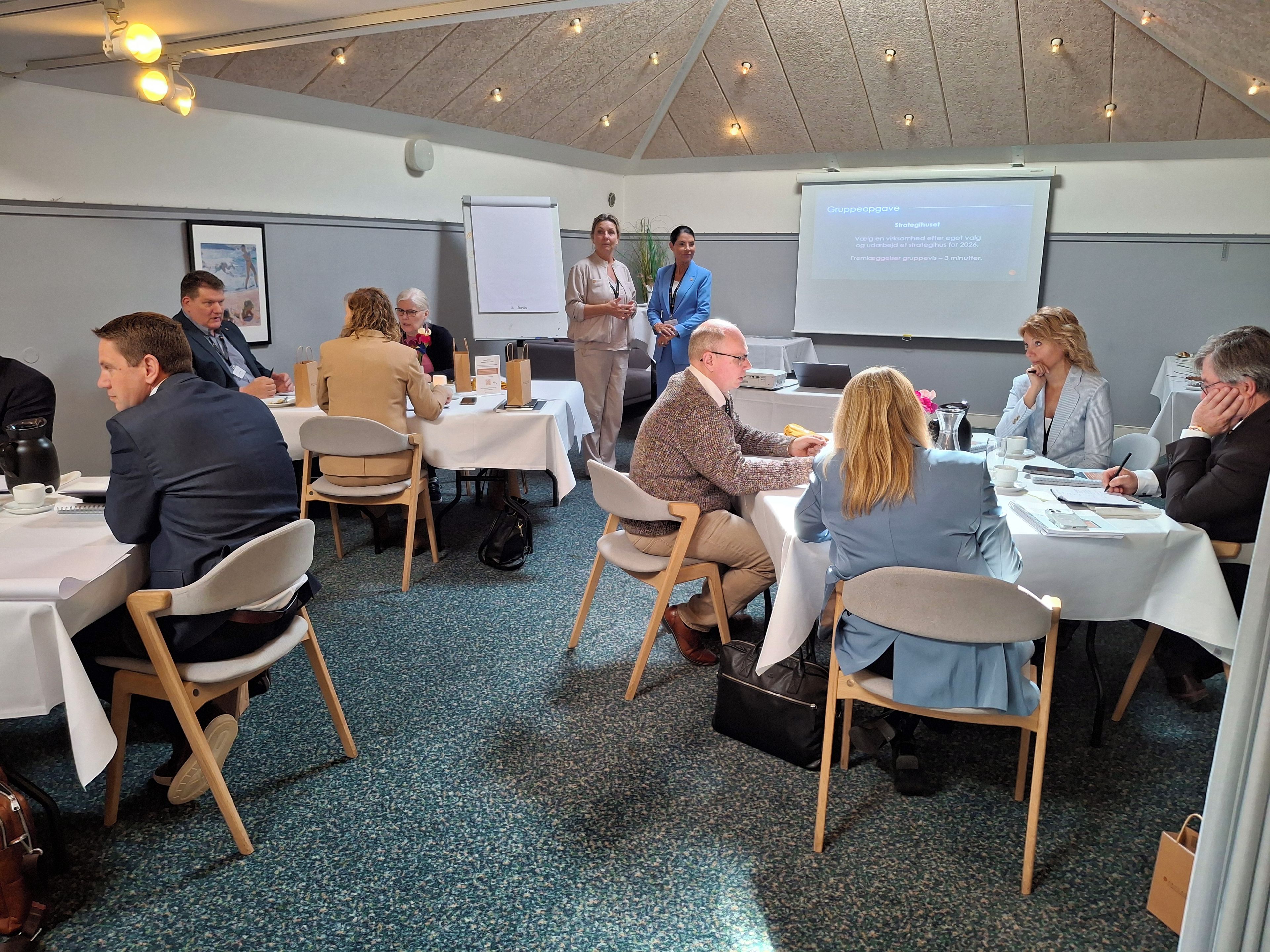 A conference room with round tables, attendees seated, and a presentation screen at the front.
