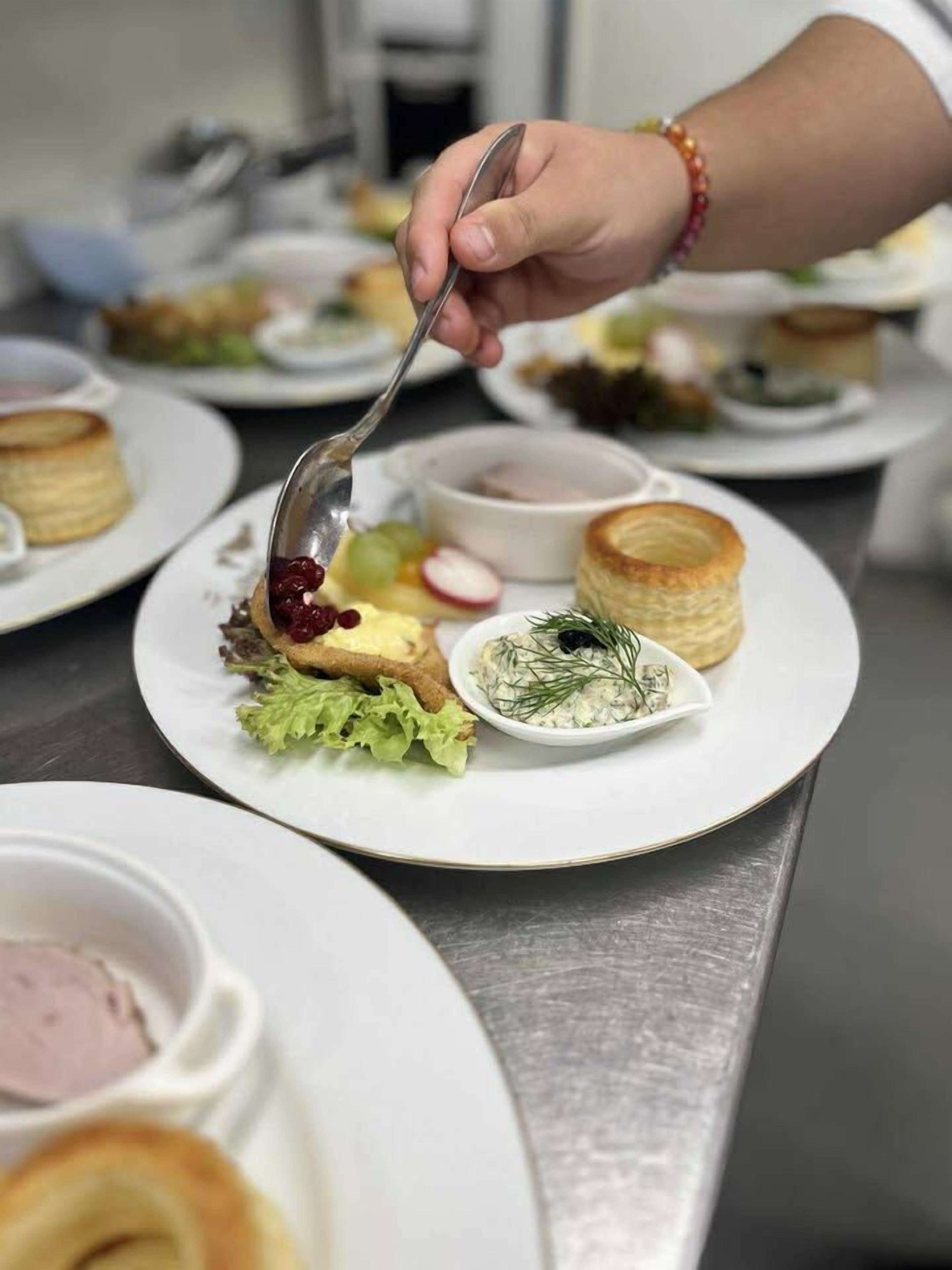 Eine Person serviert Essen von einem weißen Teller mit einem Löffel.