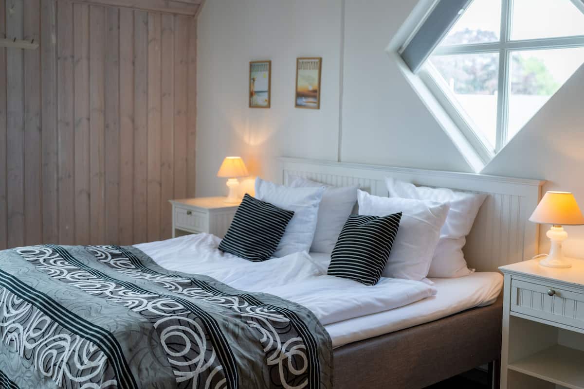 A bedroom with a bed, two bedside tables, a window, and two wall-mounted pictures.