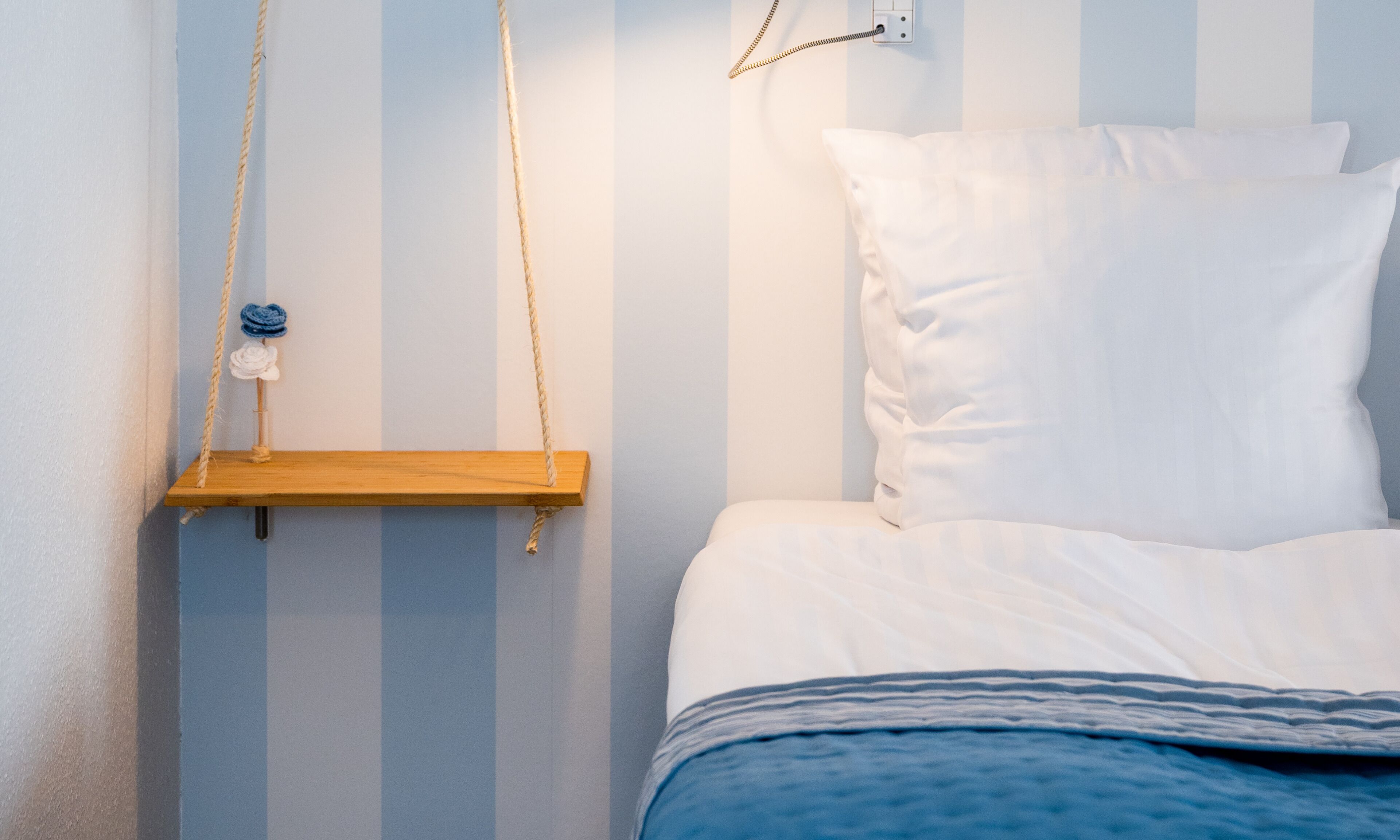 A bed with white bedding, a wooden bedside table, and a wall-mounted telephone.