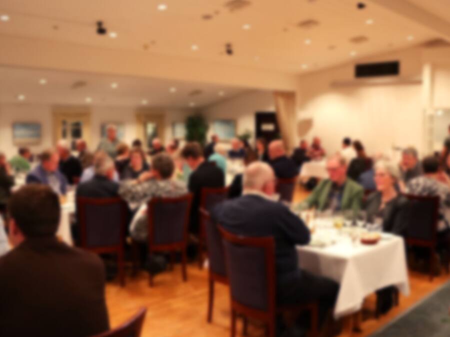 A large indoor gathering with people seated at tables, likely in a conference or banquet hall.