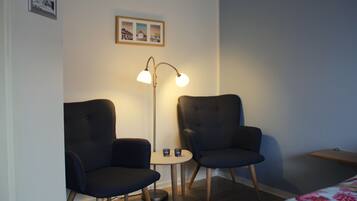 A room with two dark armchairs, a small round table, a floor lamp, and a framed picture on the wall.