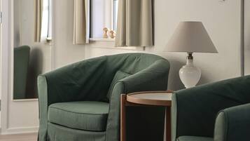 Una habitación con dos sillones verdes, una mesita redonda y una lámpara.