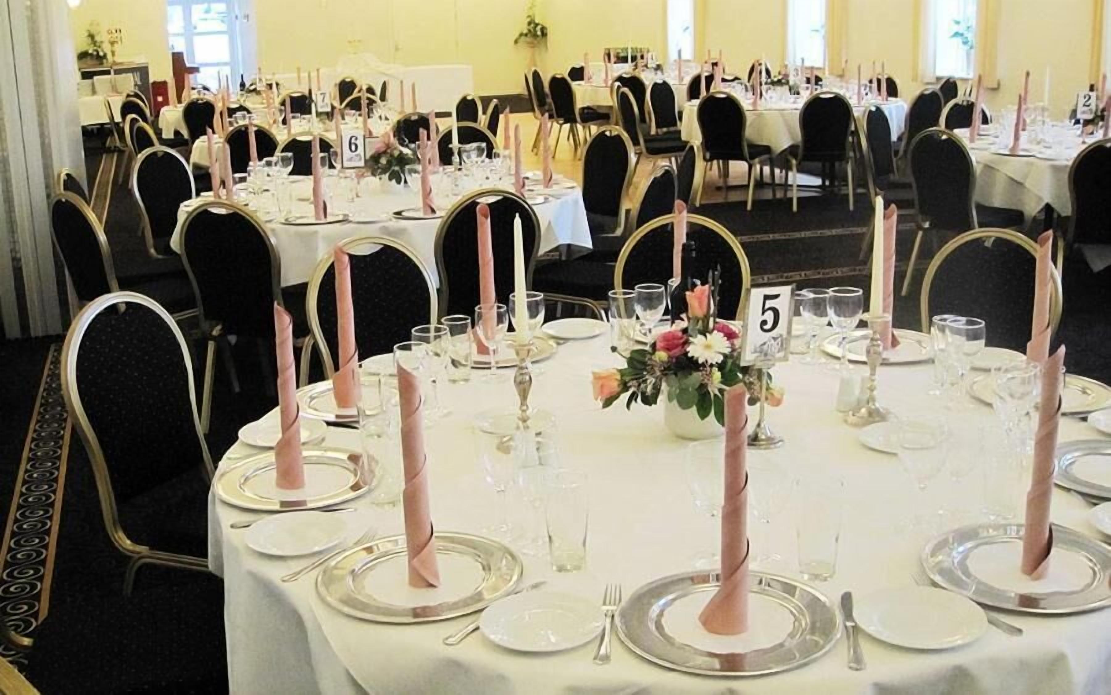 A banquet hall with round tables set for a formal event, each with numbered place cards, candles, and floral centerpieces.