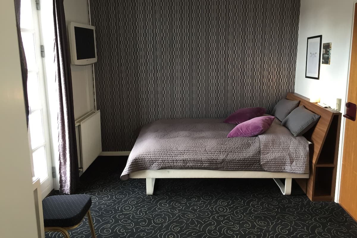 A bedroom with a bed, a small seating area, a radiator, and a wall-mounted TV.