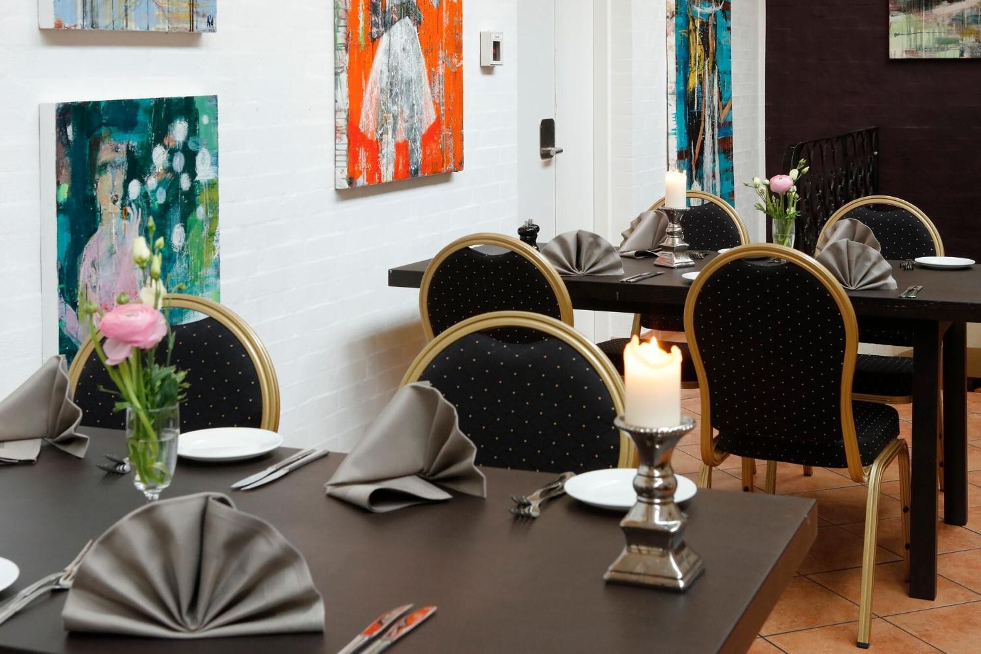 A dining area with a table set for four, featuring black chairs with gold accents, a candle centerpiece, and artwork on the walls.