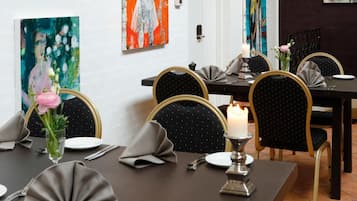 A dining area with a table set for four, featuring black chairs with gold accents, a candle centerpiece, and artwork on the walls.