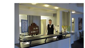 Ein Hotelrezeptionsschalter mit schwarzer Theke, einem gerahmten Schild und einer Vase mit gelben Blumen.