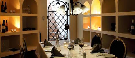 Un comedor con una mesa preparada para cuatro, copas de vino y botellas en estanterías.