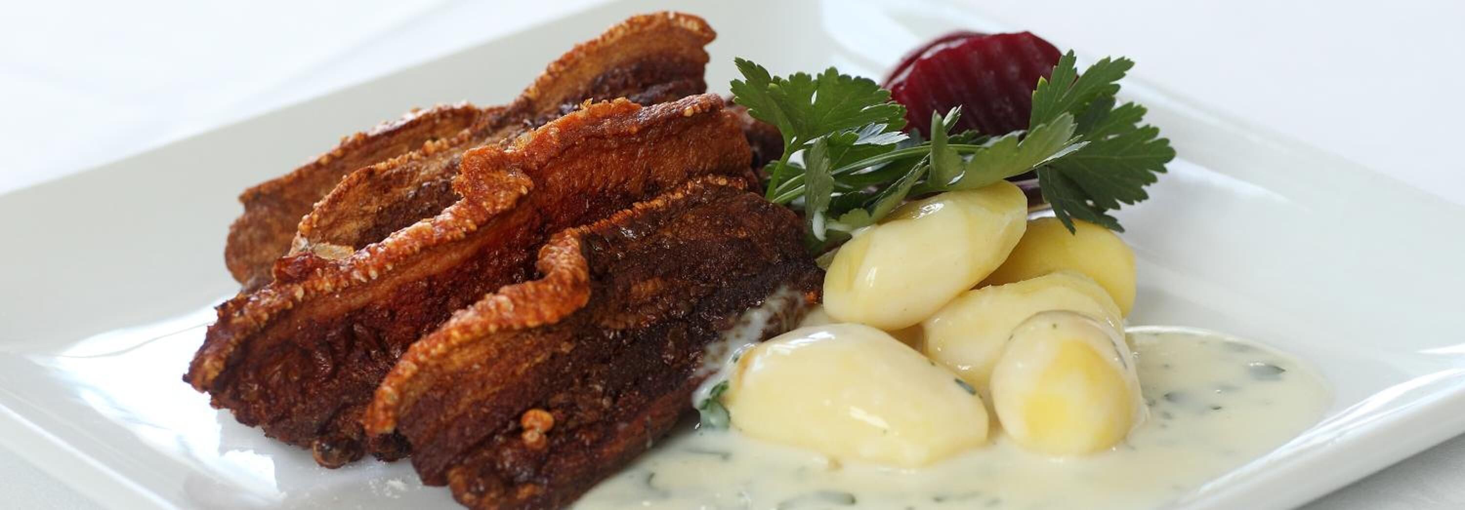 Een bord met gebakken vlees, gekookte aardappelen en garnering.